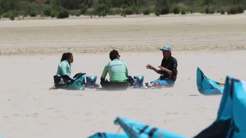 Instructor certificado enseñando la teoría del viento y seguridad a dos alumnos en la arena para el curso IKO Nivel 1 en Tarifa.
